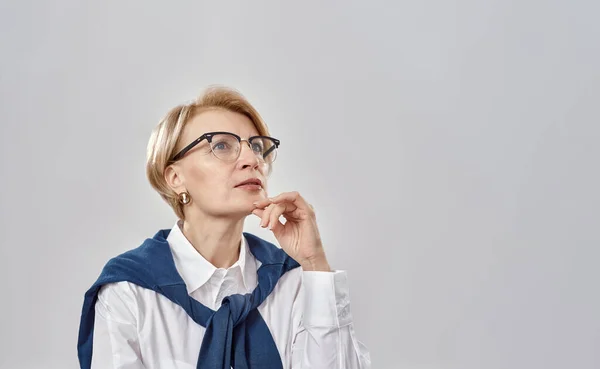 Retrato de una elegante mujer caucásica de mediana edad con atuendo de negocios y gafas que tienen un aspecto serio y reflexivo mientras posan aislados sobre un fondo gris —  Fotos de Stock