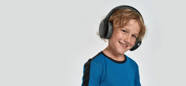 Portret szczęśliwego chłopca w sportowej odzieży i słuchawki uśmiechnięte do kamery podczas pozowania, stojące odizolowane na białym tle — Zdjęcie stockowe