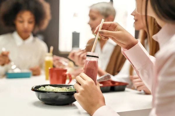 Κοντινό πλάνο ενός υγιεινού φαγητού με ένα smoothie να πίνει από μια νεαρή γυναίκα που κάθεται σε ένα τραπέζι κατά τη διάρκεια ενός επαγγελματικού γεύματος — Φωτογραφία Αρχείου