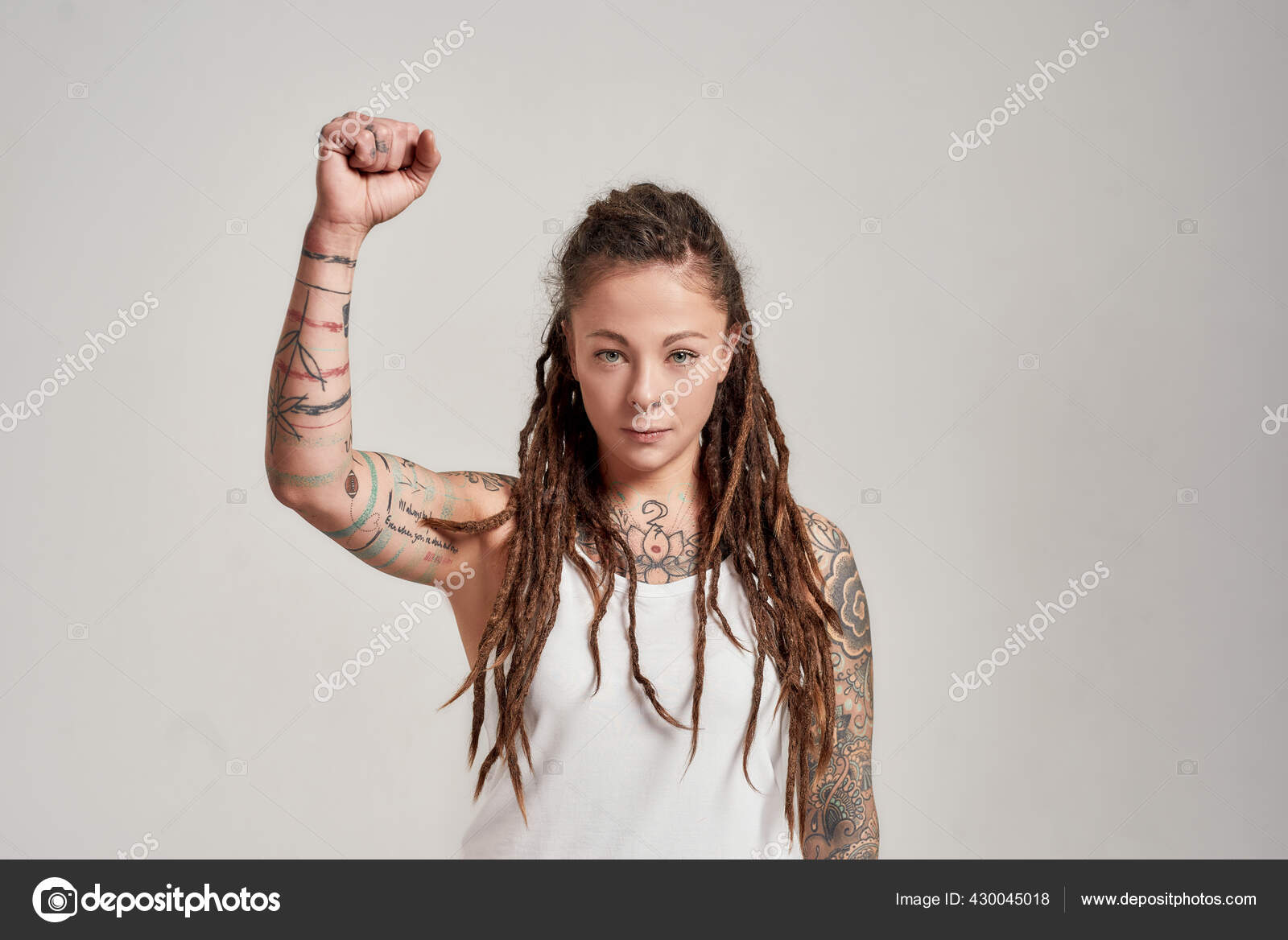 年轻纹身的高加索女人的画像 她身穿白衬衫 头戴恐惧的头发 看着相机 举起胳膊 在灰色的背景下显得孤立无援 图库照片 C Lanastock 年轻纹身的高加索女人的画像 她身穿白衬衫 头戴恐惧的头发 看着相机 举起胳膊 在灰色的背景下显得孤立无援 图库照片 C Lanastock