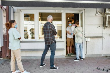 Maske takan, sırada bekleyen, kuyrukta bekleyen, koronavirüs kilitlenmesi sırasında çiçekçiden siparişlerini almak için sosyal mesafeye saygılı insanların tam boy görüntüsü.