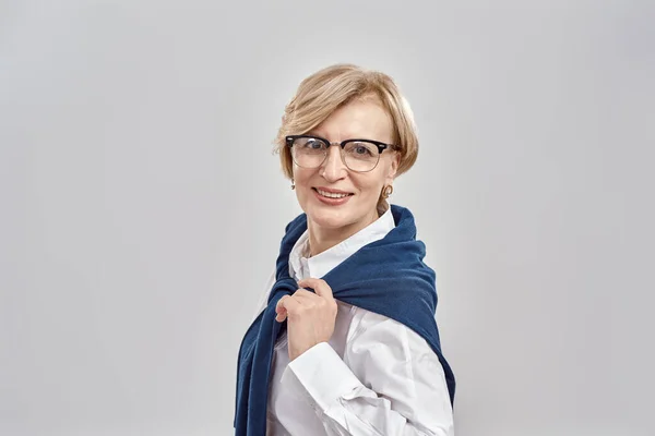 Retrato de una elegante mujer caucásica de mediana edad con atuendo de negocios y gafas sonriendo a la cámara mientras posa aislada sobre un fondo gris —  Fotos de Stock
