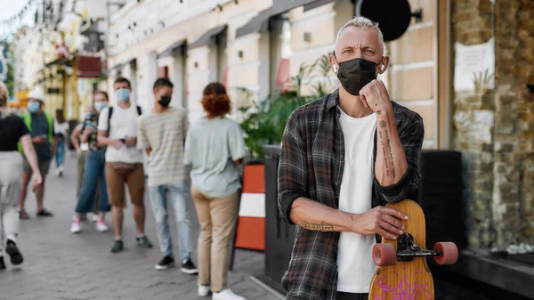 Portret van een man van middelbare leeftijd die een masker draagt met longboard, kijkend naar de camera terwijl hij wacht om zijn afhaalbestelling op te halen bij het ophaalpunt tijdens de afsluiting. — Stockfoto