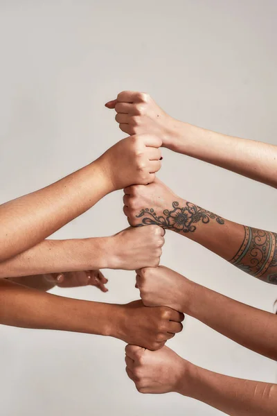 Acercamiento de manos de diversas mujeres poniendo sus puños uno encima del otro como un equipo aislado sobre fondo gris. Concepto de unidad racial y relaciones en la sociedad Imagen de archivo