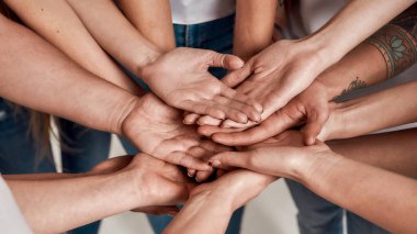 Çeşitli kadınlar bir takım gibi avuçlarını birbiri üzerine açıp el ele tutuşuyorlar. Destek kavramı, ırk birliği ve toplumsal ilişkiler