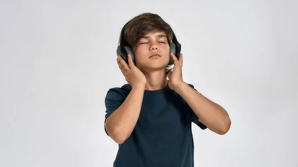 Menino esportivo em sportswear vestindo fones de ouvido, ouvindo música, de pé com os olhos fechados isolado sobre fundo branco — Fotografia de Stock