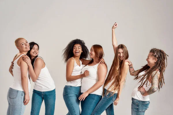 Gruppo di sei belle e diverse giovani donne che indossano camicia bianca e jeans di jeans che si divertono, ridendo mentre posano insieme isolate su sfondo grigio — Foto Stock