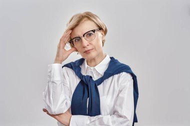 İş elbisesi ve gözlük takan zarif orta yaşlı beyaz kadın portresi. Gri arka planda izole bir şekilde poz verirken kameraya düşünceli görünüyor.