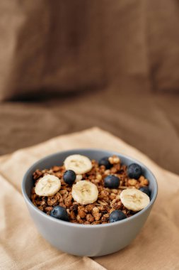 Ev yapımı tahıl gevreğini fındık, bal, yabanmersini, muz ve diğer doğal malzemelerle kaplayıp kahverengi arka planda servis edin.