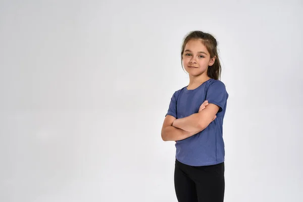 Pequeña niña deportiva en ropa deportiva mirando a la cámara, mientras está de pie con los brazos cruzados aislados sobre fondo blanco —  Fotos de Stock