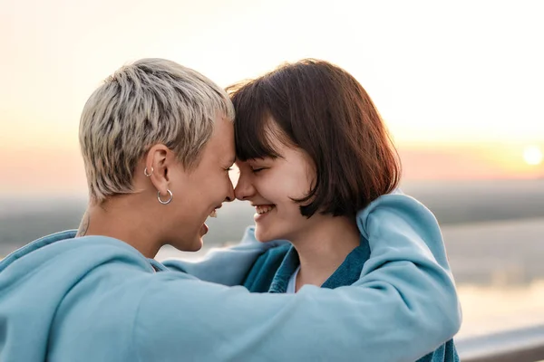 Close up of young loving lesbian couple hugging, laughing before kiss while admiring the sunrise together — Stock Photo, Image