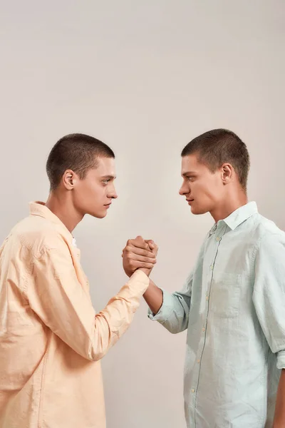 Tiro vertical de jovens irmãos gêmeos caucasianos olhando um para o outro, de mãos dadas enquanto estavam de pé face a face isolados sobre fundo bege — Fotografia de Stock