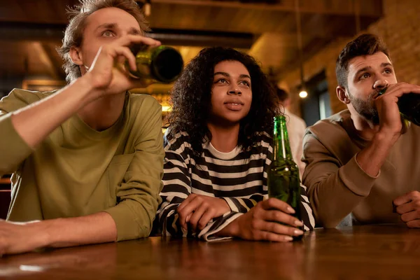 Enjoying the game. Friends in the bar watching sports match on TV together, drinking beer and cheering for team. People, leisure, friendship and entertainment concept