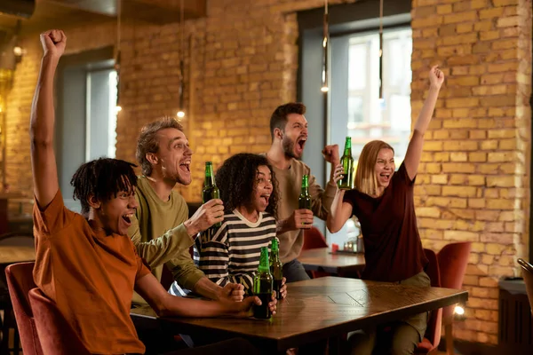 Boldog barátok a bárban együtt nézik a sportmeccset a TV-ben, söröznek és szurkolnak a csapatnak. Emberek, szabadidő, barátság és szórakozás fogalma — Stock Fotó
