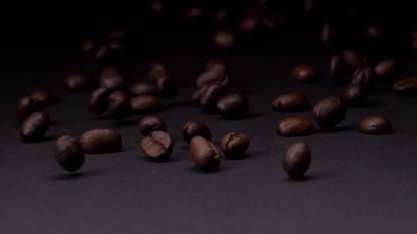 Donker en verfijnd. Slow motion shot van geroosterde bruine koffiebonen rollen, vallen op donkere achtergrond. Koffie granen close-up 4K video. — Stockvideo