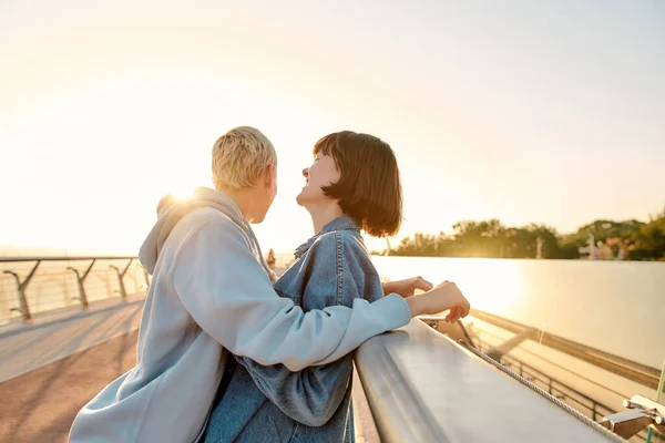 Divertidos juntos. Casal lésbico rindo, de pé juntos, apoiando-se na ponte e assistindo o nascer do sol. Homossexualidade, LGBT e conceito de amor — Fotografia de Stock