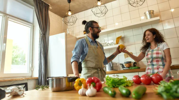 Ζευγάρι ετοιμάζεται υγιεινό γεύμα μαζί στην κουζίνα. Ιταλός μάγειρας κοιτάζει την κοπέλα του ενώ παίρνει πιπέρι. Νεαρή γυναίκα με ποδιά χαμογελάει, τον βοηθάει στην κουζίνα. — Φωτογραφία Αρχείου