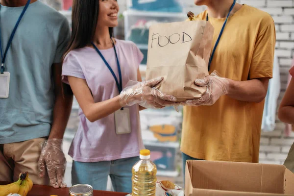 貧しい人々のための寄付を梱包しながら、食糧と紙袋を保持する男性と女性のボランティアの作物のショット,慈善財団で働く若いチーム — ストック写真