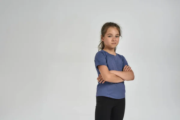 Pequeña niña deportiva en ropa deportiva mirando a la cámara, mientras está de pie con los brazos cruzados aislados sobre fondo blanco —  Fotos de Stock