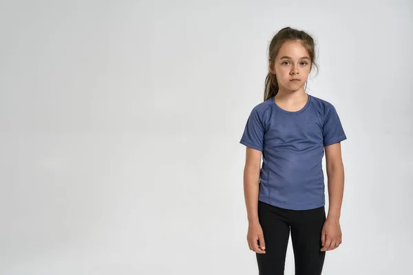 Pequena criança menina esportiva em sportswear olhando para a câmera, enquanto em pé isolado sobre fundo branco — Fotografia de Stock