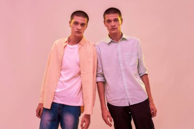 İki beyaz ikiz kardeş, açık pembe arka planda izole bir şekilde fotoğraf çektirirken kameraya bakıyorlar.