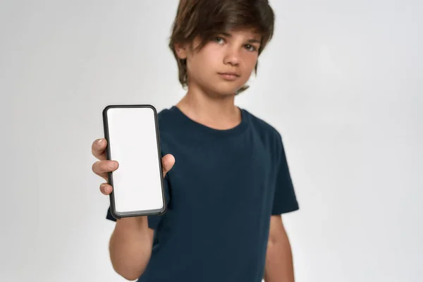 Niño pequeño deportivo en ropa deportiva sosteniendo, mostrando teléfono inteligente con pantalla en blanco, de pie aislado sobre fondo blanco — Foto de Stock