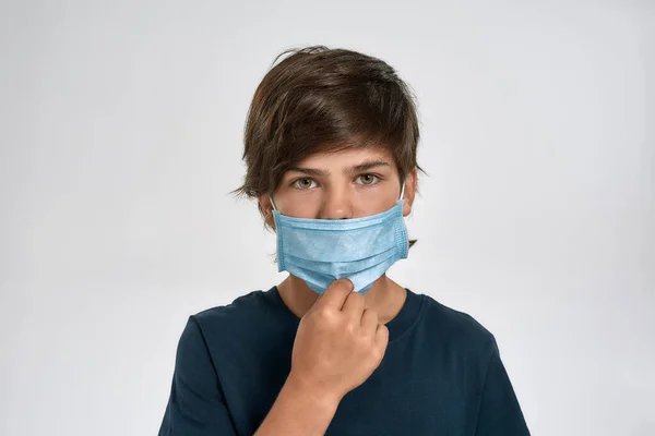 Retrato de niño pequeño deportivo en ropa deportiva usando, ajustando la máscara médica, mirando a la cámara, de pie aislado sobre fondo blanco —  Fotos de Stock