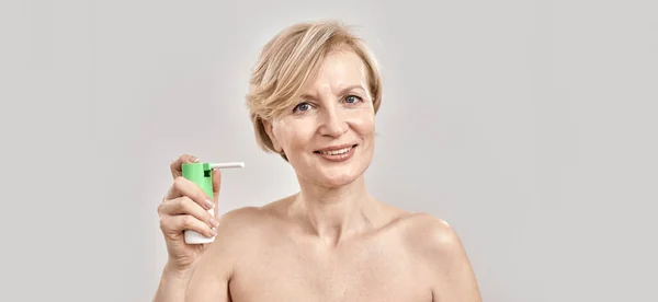 Portrait of attractive middle aged woman smiling at camera and holding throat spray, standing isolated over grey background — Stock Photo, Image