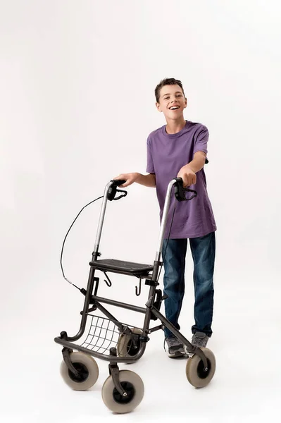 Полнометражный снимок счастливого подростка-инвалида с церебральным параличом, улыбающегося в камеру, шагающего с изолированным ходячим на белом фоне — стоковое фото