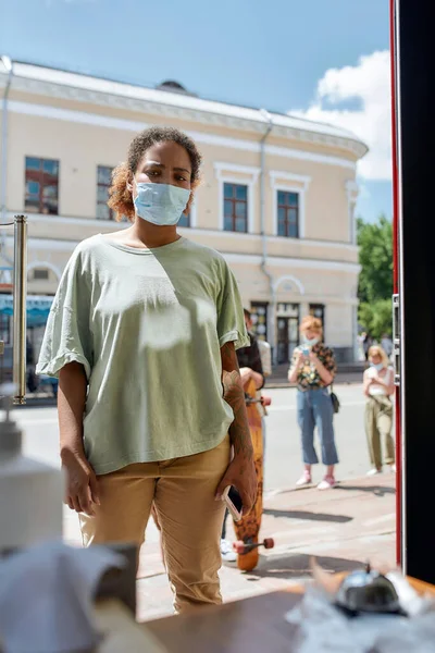 Mujer afroamericana joven con máscara esperando para recoger su pedido o compra desde el punto de recogida durante el bloqueo coronavirus — Foto de Stock