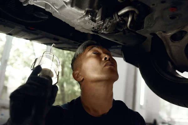 Mecánico mirando hacia arriba en la parte inferior auto aligerado por la linterna — Foto de Stock