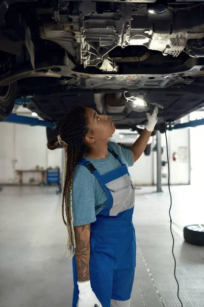 Joven afroamericano chica mecánica mirando en la parte inferior del coche — Foto de Stock