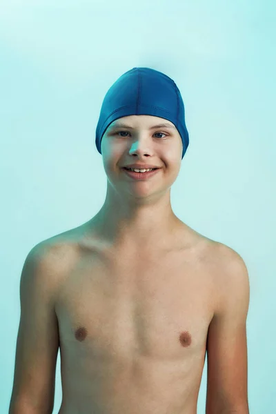 Portré a Down-kóros fiúról, aki fürdősapkában mosolyog a kamera előtt, miközben türkiz háttér felett elszigetelve pózol. Úszás rehabilitációs koncepció — Stock Fotó