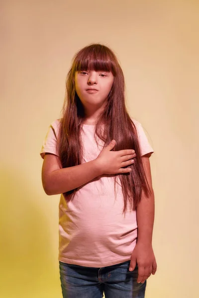 Portrait of disabled girl with Down syndrome looking at camera while posing isolated over creative yellow background — Stock Photo, Image