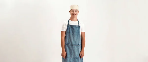 Niño discapacitado vestido como cocinero en delantal y sombrero sonriendo a la cámara mientras posa aislado sobre fondo blanco — Foto de Stock