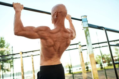 Sporcu, çapraz çubukta geniş tutuşu çekiyor.