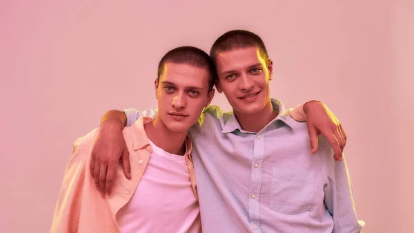 Справжні друзі. Портрет двох молодих кавказьких чоловіків, братів-близнюків у повсякденному одязі, які обіймаються і дивляться на камеру — стокове фото