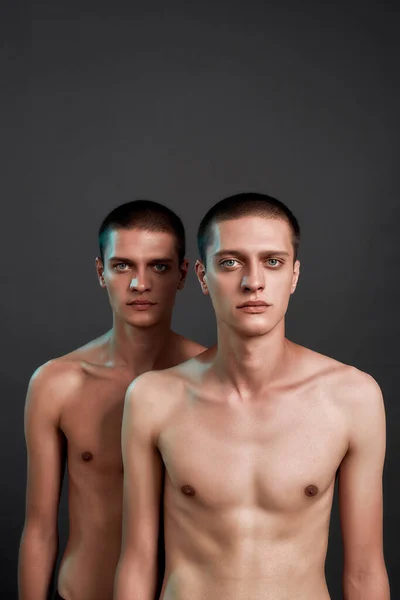 二人の若い白人の半分裸の双子の兄弟の撮影スタジオでポーズをとりながらカメラを見て,灰色の背景の上に隔離された立って — ストック写真