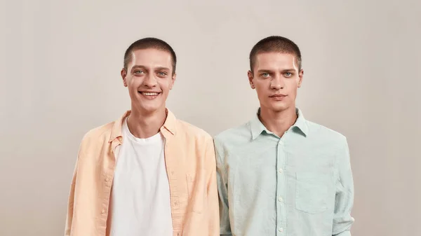 Porträtt av två unga tvillingbröder bär casual kläder tittar på kameran framför kameran samtidigt poserar tillsammans isolerad över beige bakgrund — Stockfoto
