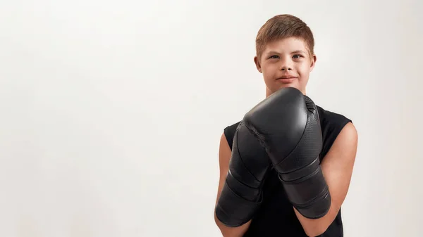 Portrait of cheerful disabled boy with Down syndrome wearing big boxing gloves, looking at camera while posing isolated over white background — Stock Photo, Image