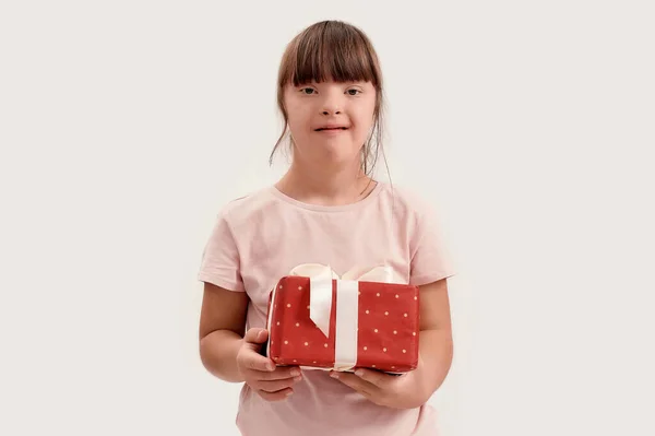 Retrato de chica discapacitada con síndrome de Down sonriendo a la cámara, sosteniendo regalo de cumpleaños mientras posando aislado sobre fondo blanco —  Fotos de Stock