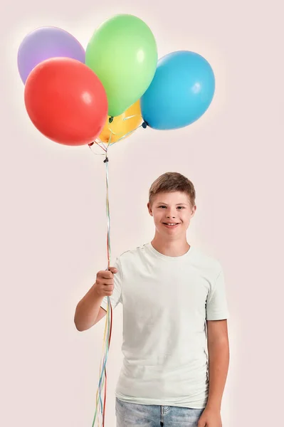 Feliz adolescente discapacitado chico con síndrome de Down sonriendo a la cámara, sosteniendo un montón de globos de colores, mientras que de pie aislado sobre fondo blanco — Foto de Stock