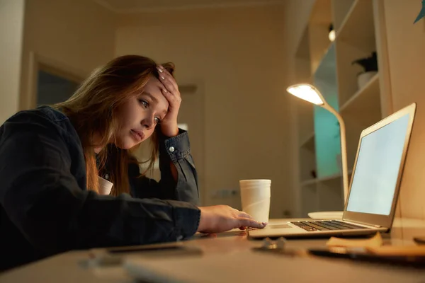 Necesito un descanso. Mujer joven cansada mirando la pantalla del ordenador portátil, sentada en su lugar de trabajo por la noche en casa. Me siento agotado. Trabajando remotamente —  Fotos de Stock