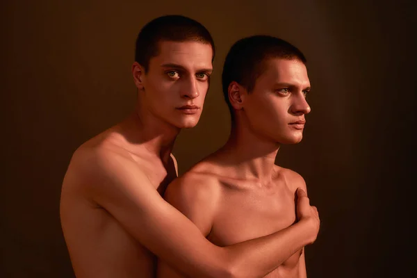 Eres la persona más cercana a mí. Dos jóvenes medio desnudos hermanos gemelos caucásicos posando juntos en el estudio, de pie aislado sobre fondo marrón —  Fotos de Stock