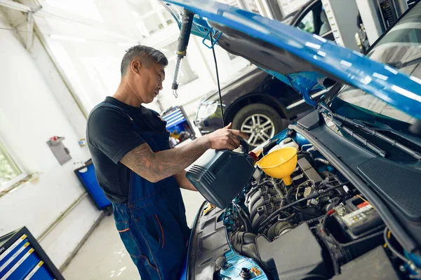 Asian man pouring engine oil standing near open hood — Stock Image Asian man pouring engine oil standing near open hood Stock Picture