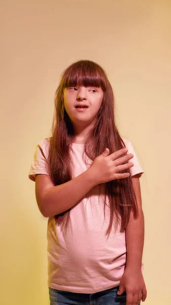Portrait of disabled girl with Down syndrome looking aside while posing isolated over creative yellow background — Stock Photo, Image