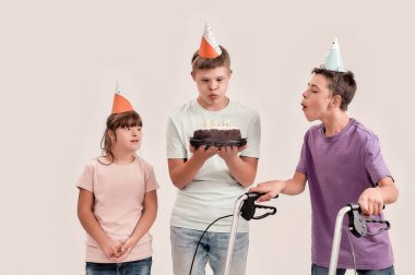 Doğum gününü doğum günü şapkalı arkadaşlarıyla birlikte kutlarken sakat bir çocuk beyaz arka planda tek başına dikiliyor.