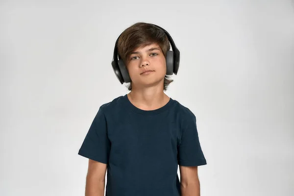 Μικρό σπορ παιδί με αθλητικά ρούχα που φοράει ακουστικά, ακούει μουσική, κοιτάζει κάμερα ενώ ποζάρει απομονωμένο σε λευκό φόντο — Φωτογραφία Αρχείου