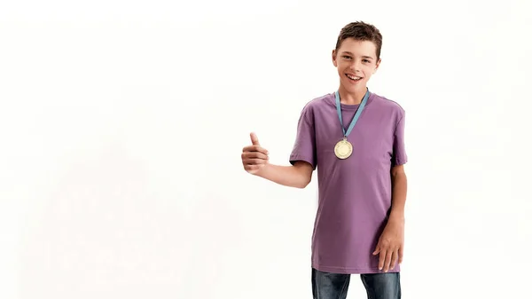 Ευτυχισμένο έφηβο ανάπηρο αγόρι με εγκεφαλική παράλυση που φοράει χρυσό μετάλλιο, χαμογελάει και δείχνει τους αντίχειρες του στην κάμερα, στέκεται απομονωμένο πάνω από λευκό φόντο — Φωτογραφία Αρχείου
