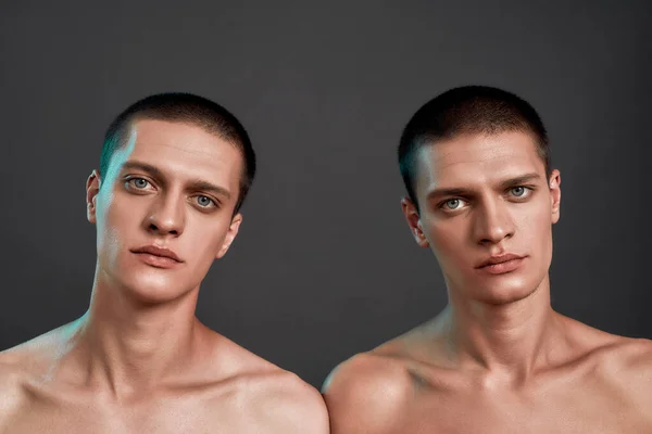 Retrato de hermanos gemelos semidesnudos jóvenes mirando a la cámara mientras están aislados sobre un fondo gris oscuro, vista frontal —  Fotos de Stock